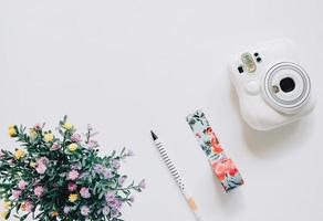 creativo piatto posare mestiere stile con immediato telecamera, penna, mascheratura nastro e fiore su bianca sfondo con copia spazio foto