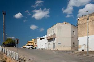 tipico strada scena di un' cittadina nel sicilia nel estate in giro mezzogiorno. case In piedi a il lato di il strada, un' strada sorge e bianca nuvole deriva attraverso il blu cielo. foto