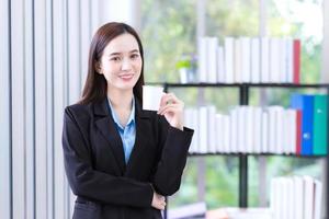 asiatico Lavorando donna nel un' nero completo da uomo detiene carta tazza per bevanda caffè nel il mattina a ufficio. foto