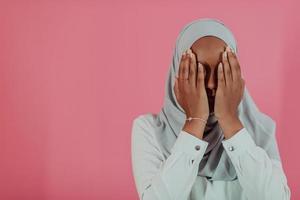moderno africano musulmano donna fa tradizionale preghiera per Dio, mantiene mani nel preghiere gesto, indossa tradizionale bianca Abiti, ha grave facciale espressione, isolato al di sopra di plastica rosa sfondo foto