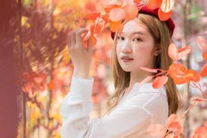 asiatico donna chi indossa bianca camicia e rosso berretto sta nel rosso-arancione partire come Forrest nel autunno.
