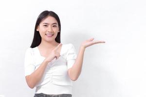 la donna asiatica con i capelli lunghi neri indossa una camicia bianca e mostra il punto per presentare qualcosa su sfondo bianco. foto