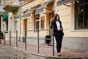 bellissima indiano donna indossare formale in posa a strada con mobile Telefono a mani. foto