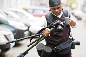 giovane professionale africano americano operatore video Tenere professionale telecamera con tripode professionista attrezzatura. afro cineoperatore indossare nero duraq fabbricazione un' video. foto