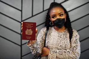 africano americano donna indossare nero viso maschera mostrare Bolivia passaporto nel mano. coronavirus nel America nazione, confine chiusura e quarantena, virus scoppio concetto. foto