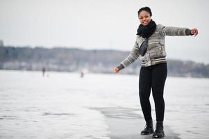 africano donna indossare nel nero sciarpa posa nel congelato ghiaccio lago, inverno giorno a Europa. foto