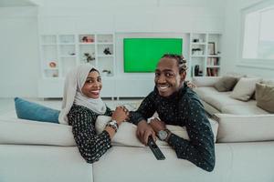africano coppia seduta su divano Guardando tv insieme croma verde schermo donna indossare islamico hijab Abiti foto