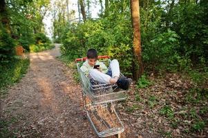 ragazzo seduta nel carrello con mobile Telefono a foresta. foto