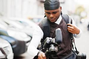 giovane professionale africano americano operatore video Tenere professionale telecamera con tripode professionista attrezzatura. afro cineoperatore indossare nero duraq fabbricazione un' video. foto