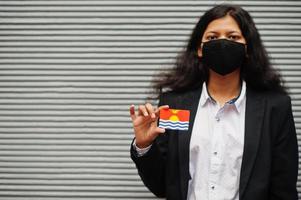 asiatico donna a formale indossare e nero proteggere viso maschera hold kiribati bandiera a mano contro grigio sfondo. coronavirus a nazione concetto. foto