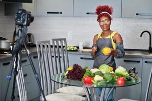 africano americano donna le riprese sua blog trasmissione di salutare cibo a casa cucina. lei tagli un' pomodoro con coltello. foto