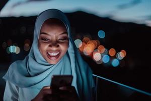 giovane musulmano donna indossare sciarpa velo su urbano città strada a notte sms su un' smartphone con bokeh città leggero nel il sfondo.
