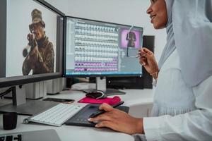 giovane afro americano moderno musulmano donna d'affari indossare un' sciarpa nel un' creativo luminosa ufficio posto di lavoro con un' grande schermo. foto