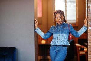 bello africano americano donna con dreadlocks nel blu elegante jeans giacca a bar. bellissimo freddo alla moda nero giovane ragazza interno. foto