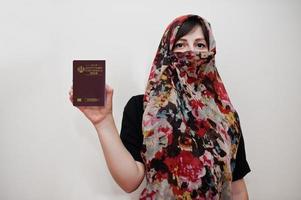 giovane arabo musulmano donna nel hijab Abiti hold islamico repubblica di mi sono imbattuto passaporto su bianca parete sfondo, studio ritratto. foto