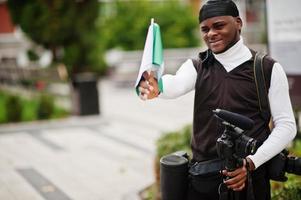 giovane professionale africano americano operatore video Tenere professionale telecamera con nigeriano bandiere nel mani. foto
