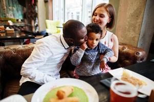 contento multietnico famiglia con ragazzo ragazzo trascorrere tempo a ristorante. relazioni di africano uomo e bianca europeo donna. foto