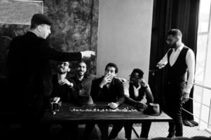 gruppo di bello retrò ben vestito uomo gangster trascorrere tempo a club. multietnico maschio laurea breve mafia festa nel ristorante, seduta di tavolo. foto