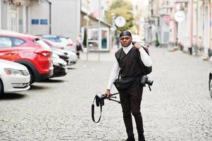 giovane professionale africano americano operatore video Tenere professionale telecamera con tripode professionista attrezzatura. afro cineoperatore indossare nero duraq fabbricazione un' video. foto
