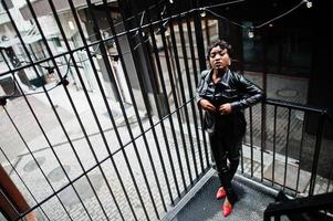 alla moda bellissimo africano americano donna in posa nel nero pelle giacca e pantaloni a strada. foto