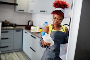 africano americano donna a casa cucina Aperto frigo e avuto latte bottiglia. foto