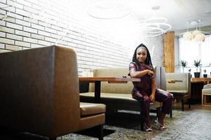 bellissimo africano americano donna nel rosso pelle costume posa a ristorante. foto