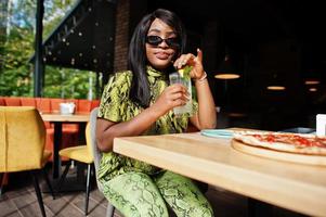 fascino africano americano donna mangiare Pizza e bevanda limonata a ristorante. foto