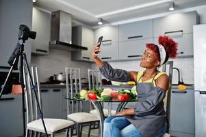 africano americano donna le riprese sua blog trasmissione di salutare cibo a casa cucina e fabbricazione autoscatto a Telefono. foto