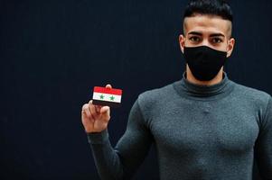 mezzo orientale uomo nel grigio dolcevita e nero viso proteggere maschera mostrare Siria bandiera isolato sfondo. foto