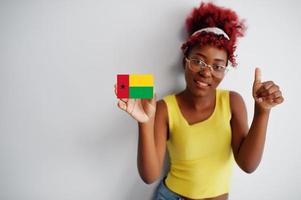 africano donna con afro capelli, indossare giallo canottiera e occhiali, hold guinea-bissau bandiera isolato su bianca sfondo, mostrare pollice su. foto