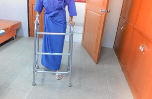 medico e assistenza sanitaria concetto, avvicinamento di femmina pazienti pratica a piedi con un' camminatore nel il ospedale . foto