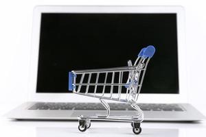 il computer portatile con un' piccolo shopping carrello, su un' bianca sfondo. selettivo messa a fuoco. copia spazio. foto