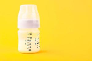 bianca plastica bambino bottiglia con pacificatore, ricco nel bambino cibo, su giallo sfondo. copia spazio. foto