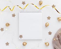 bianca foglio di taccuino su bianca tavolo con stelle, Natale palle e festivo ghirlanda. concetto pianificazione, desiderio elenco per il nuovo anno foto