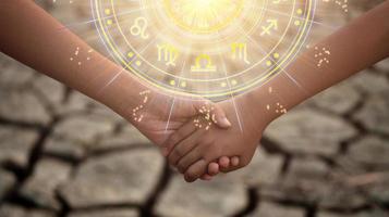 giovane ragazzo e ragazza Tenere mani nel il secco suolo con il sole leggero passaggio attraverso il mani avere astrologico simboli. foto