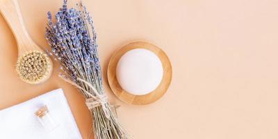 flatlay composizione con lavanda fiori e naturale cosmetico prodotti. biologico terme cosmetico. massaggio viso spazzola, sapone sbarra, mare sale e bambù asciugamano su un' beige sfondo. bandiera foto