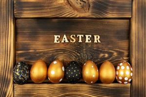 Pasqua festivo sfondo. superiore Visualizza di Pasqua uova colorato con d'oro dipingere e iscrizione nel inglese Pasqua. di legno lettere su buio legna sfondo. vario tratteggiata design foto