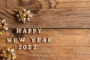 contento nuovo anno 2022 iscrizione fatto con di legno lettere decorato festivo d'oro fiocchi su di legno sfondo con copia spazio. saluto carta per nuovo anno celebrazione foto