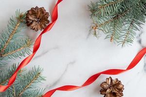 christmass e nuovo anno saluto carta con copia spazio. blu conifera rami, coni e rosso satinato nastro disposte su bianca marmo sfondo foto