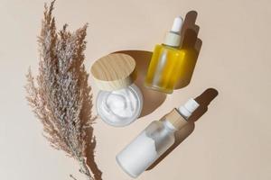 impostato di naturale anti invecchiamento pelle cura cosmetici con asciutto canne brunch su beige sfondo. bellezza viso olio, essenziale olio e viso crema nel un' bicchiere senza marchio pacchetto foto