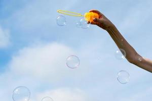 Childs mano Tenere un' bacchetta magica per soffiaggio sapone bolle contro il blu cielo su un' soleggiato estate giorno. foto