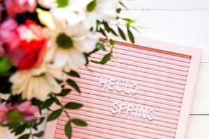 inglese testo Ciao primavera su un' rosa lettera tavola con fioritura fiori. lettera tavola su bianca di legno sfondo foto