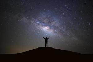 paesaggio con latteo modo galassia, stellato notte cielo con stelle e silhouette di un' in piedi sportivo uomo con sollevato su braccia su alto montagna. foto