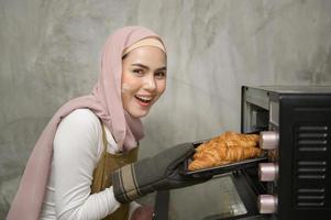 giovane bellissimo musulmano donna è cottura al forno nel sua cucina , forno e caffè negozio attività commerciale foto