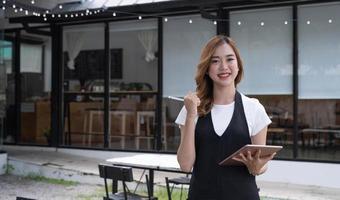 attraente bellissimo giovane asiatico femmina ristorante o caffè negozio cameriera notando un' clienti ordine su un' digitale tavoletta. foto