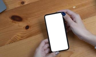mano donna utilizzando un' telefono, vuoto schermo inteligente Telefono e computer su di legno tavolo superiore Visualizza. foto