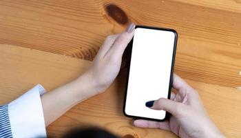 mano donna utilizzando un' telefono, vuoto schermo inteligente Telefono e computer su di legno tavolo superiore Visualizza. foto