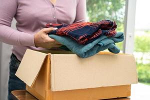 tenendo in mano una scatola per la donazione di vestiti con vestiti usati e una bambola a casa per sostenere l'aiuto ai poveri nel mondo. foto