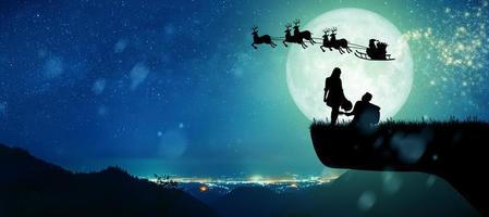 silhouette di babbo natale di notte natale con coppia che balla sotto la luna piena. foto