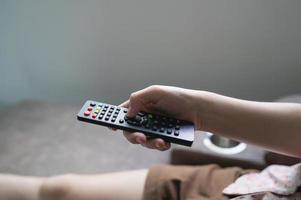 vicino su televisione a distanza controllo nel giovane donna rosa camicia mani puntamento per tv impostato e svolta esso su o spento. Selezionare canale Guardando tv su divano a casa nel il vivente camera relax. foto